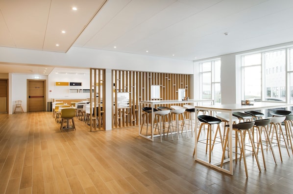 Un espacio de oficina moderno con suelo de madera, paredes blancas y una zona de bar con taburetes.