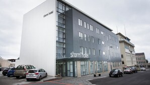 Un hotel moderno con un llamativo letrero que dice 'storm hotel', un estacionamiento con varios coches y un cielo despejado.