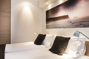 Un dormitorio con cama, almohadas, una mesita de noche, una lámpara y un cuadro grande con una escena de playa.