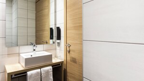 Un baño moderno con un lavamanos blanco, tocador de madera y un espejo grande.