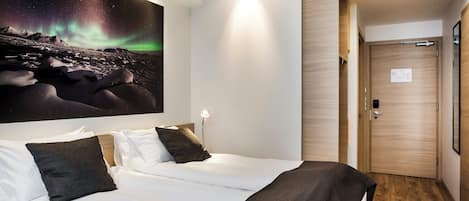 Habitación de hotel con una cama, un mural del cielo nocturno, una puerta de madera y una mesita de noche con una lámpara.