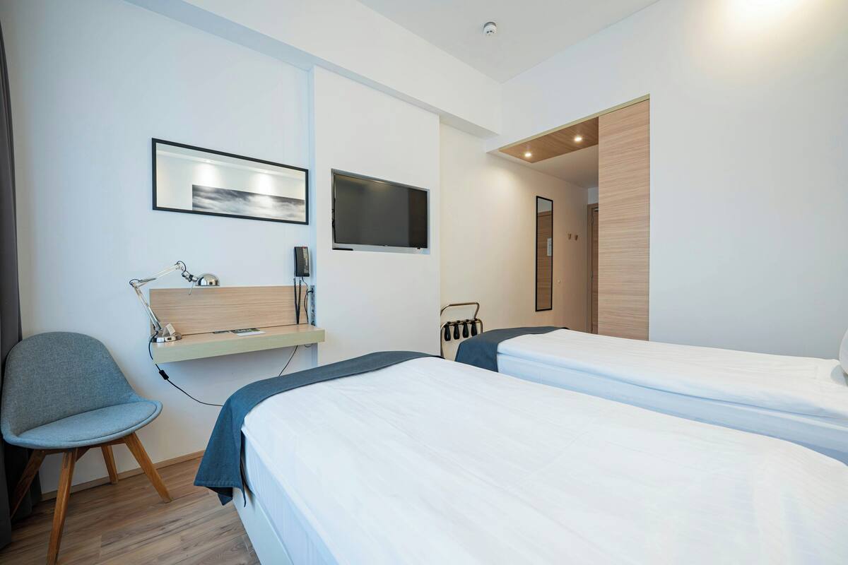 Una habitación de hotel moderna con dos camas, un escritorio con una computadora, una silla y un televisor montado en la pared.