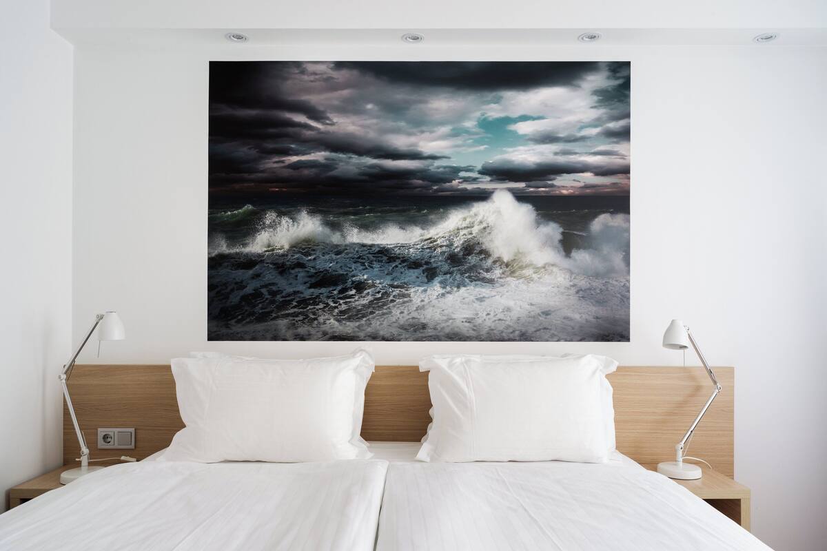 Une chambre avec un grand tableau représentant une vague océanique au mur, une tête de lit en bois et deux lampes de chevet.