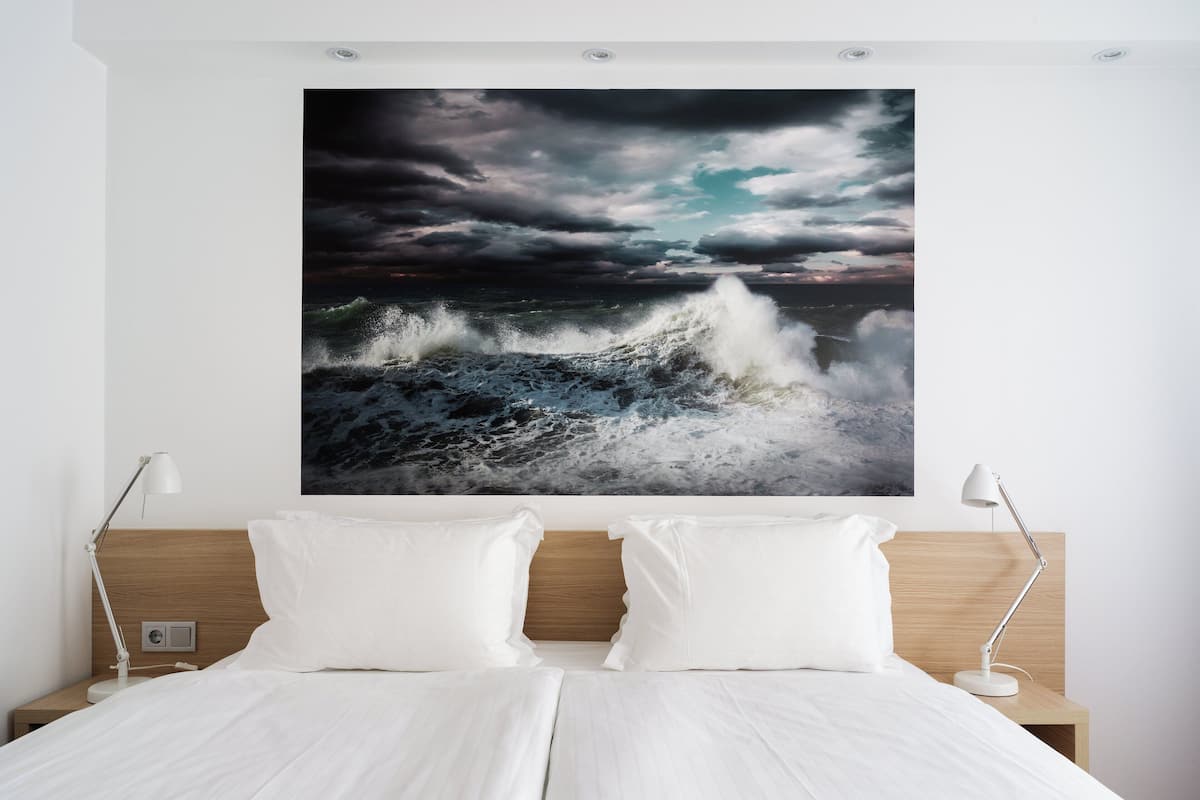Un dormitorio con un cuadro grande de una ola oceánica en la pared, un cabecero de madera y dos lámparas de noche.