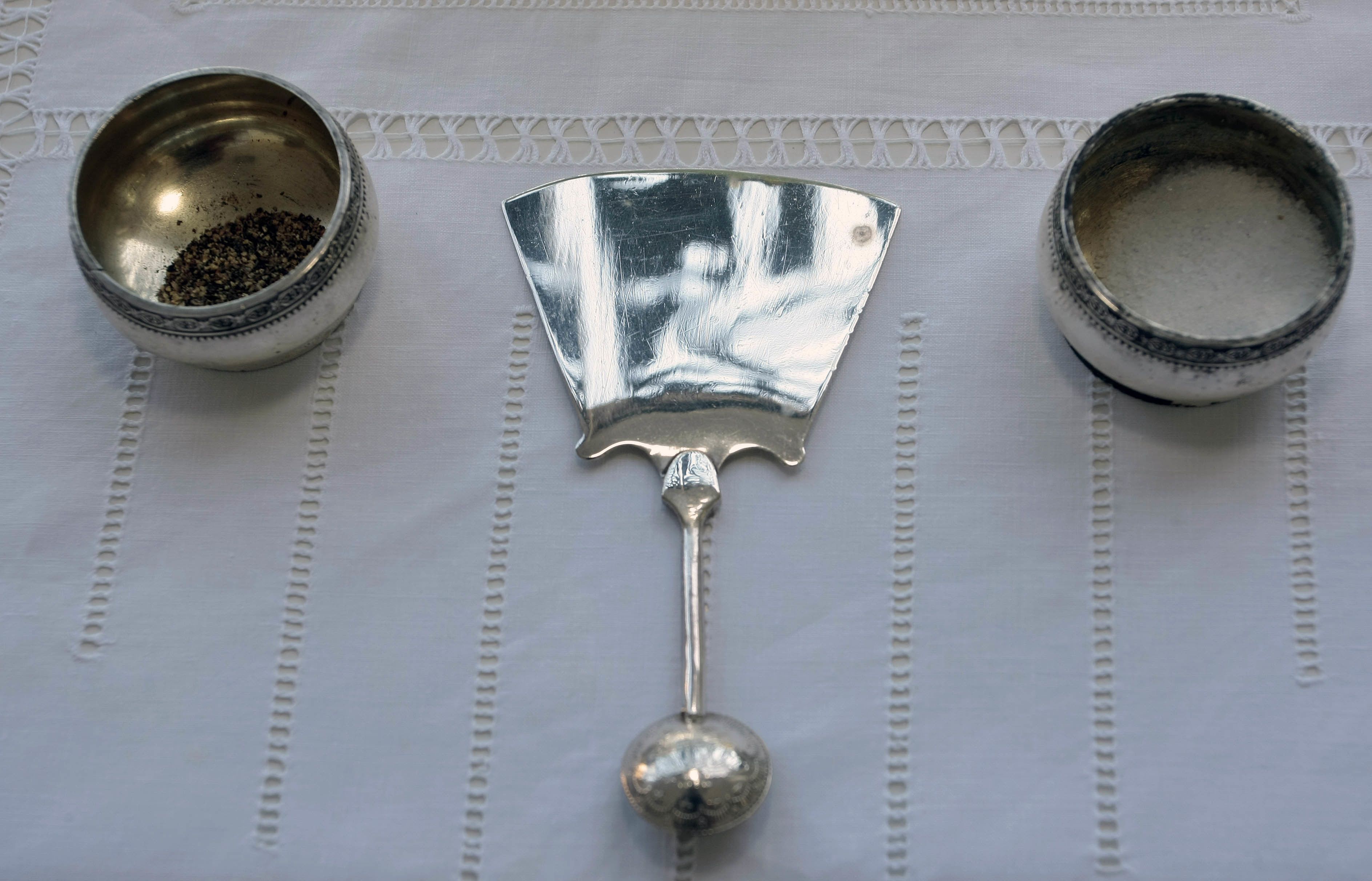 Three metal containers with a decorative handle, placed on a white tablecloth with a lace pattern.
