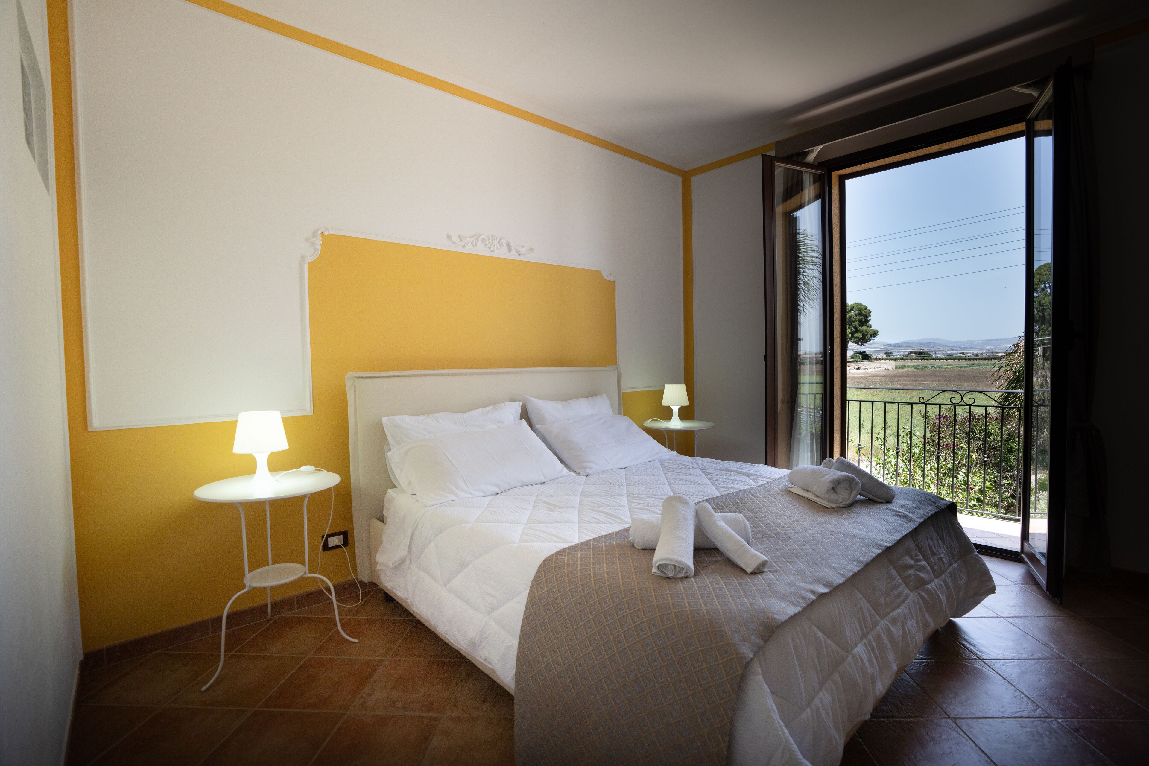Habitación de hotel con una cama, una mesita de noche con lámpara y vistas al exterior.