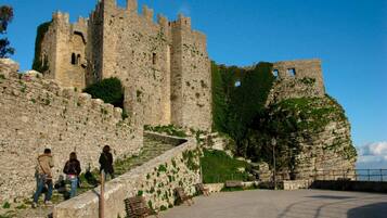 Un castillo de piedra histórico con almenas, un camino empedrado y bancos.