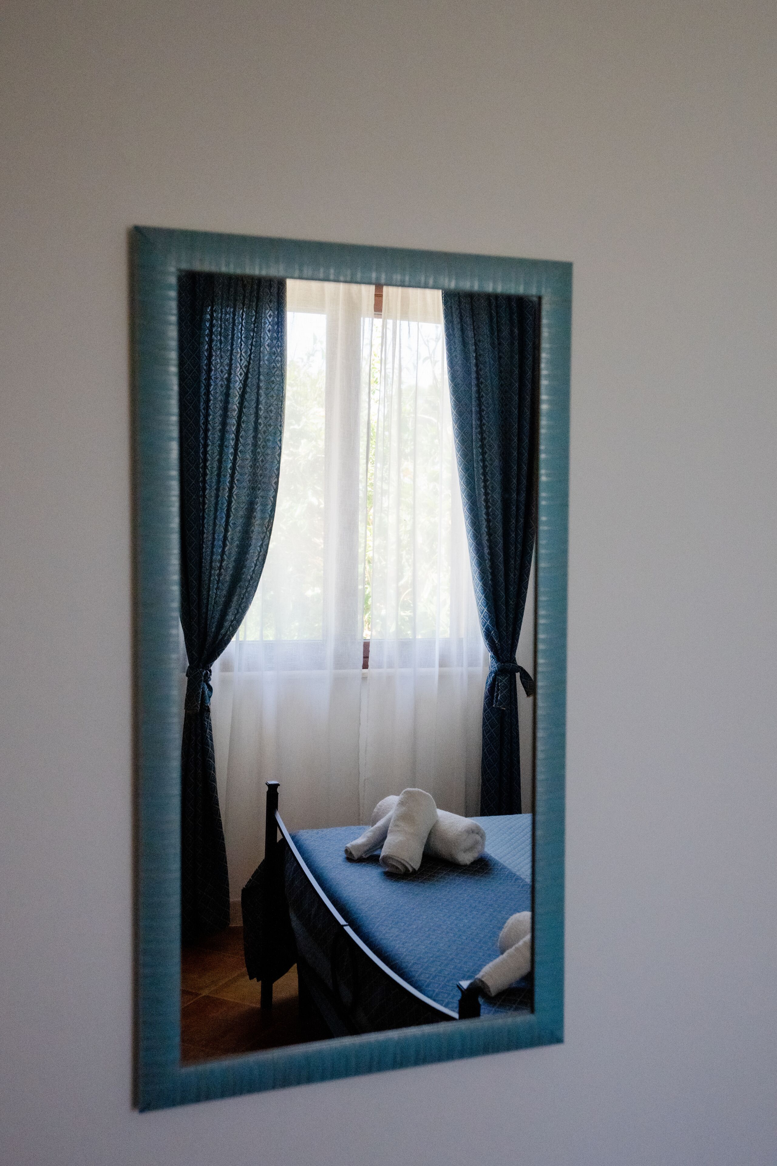 Una habitación con una cama, una ventana con cortinas y un espejo en la pared.