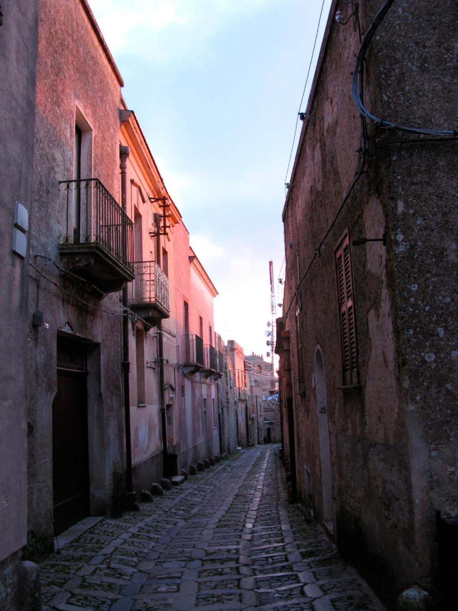 A narrow cobblestone street flanked by old buildings with balconies and shutters.