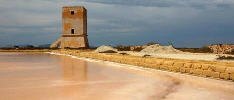 Un paisaje costero con una laguna salada, una estructura pequeña similar a una torre y una playa arenosa.