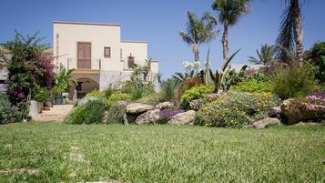 A two-story building with a flat roof, a balcony, and a garden with various plants and flowers.