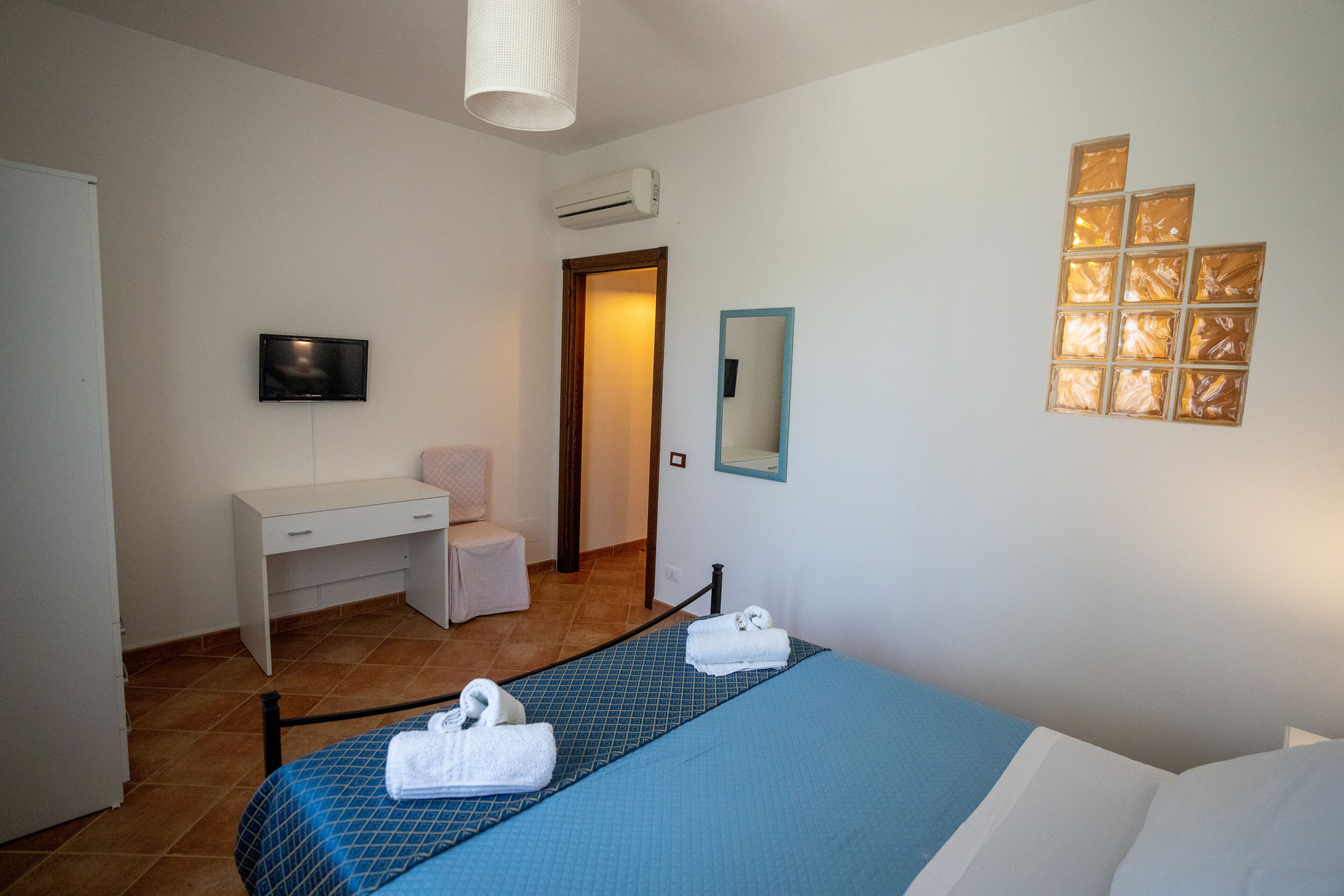A hotel room with a bed, a desk, a chair, a TV, and a mirror.