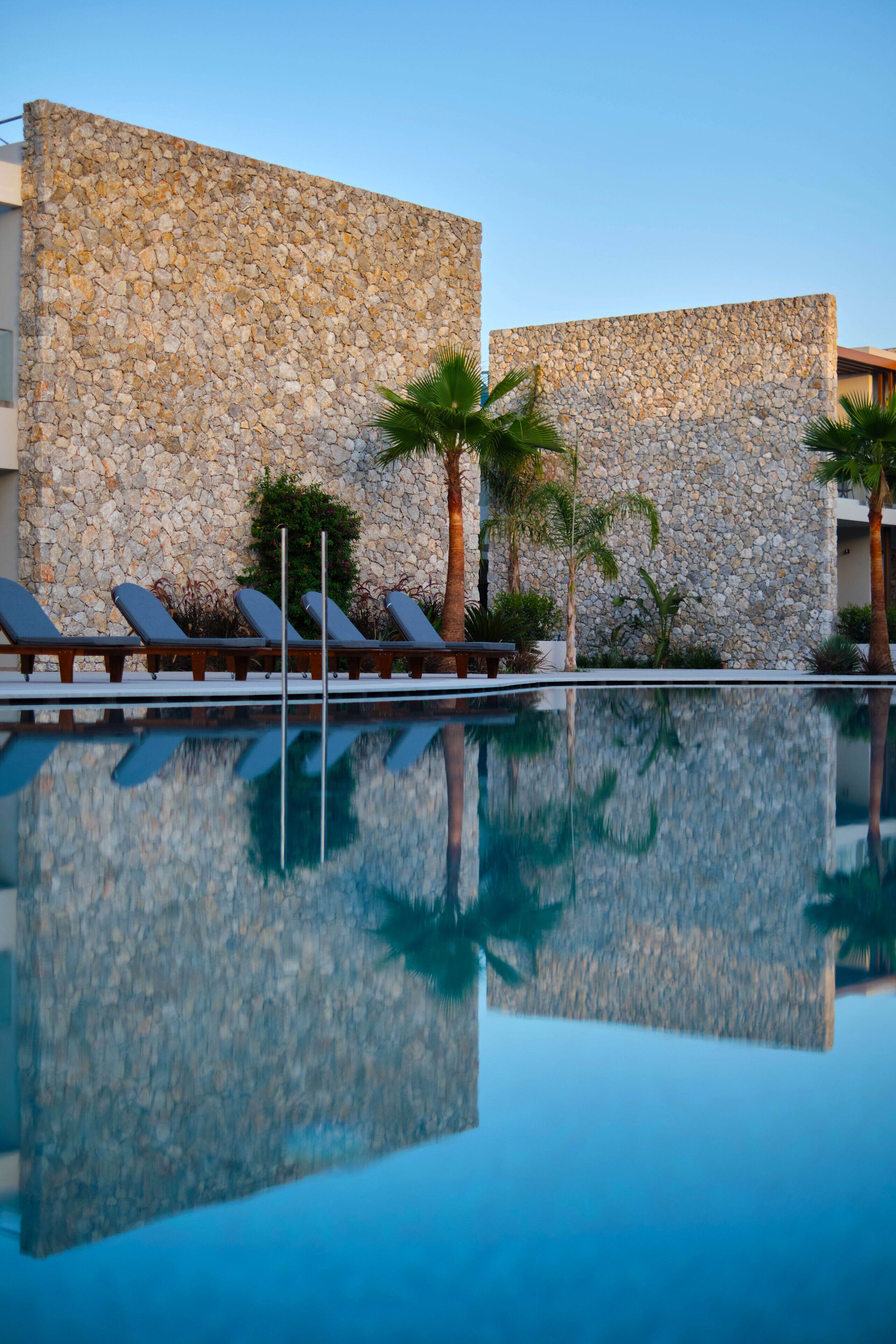 A pool with lounge chairs and palm trees, surrounded by stone walls.