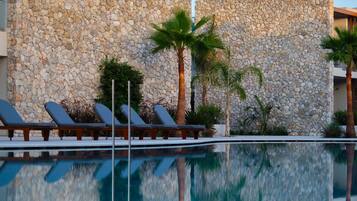 A pool with lounge chairs and palm trees, surrounded by stone walls.