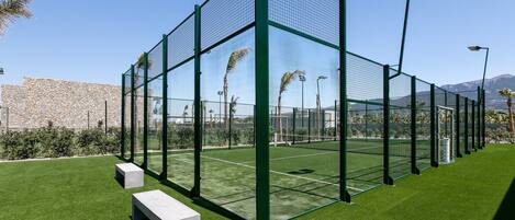 A tennis court with a green fence, artificial grass, and a stone wall in the background.