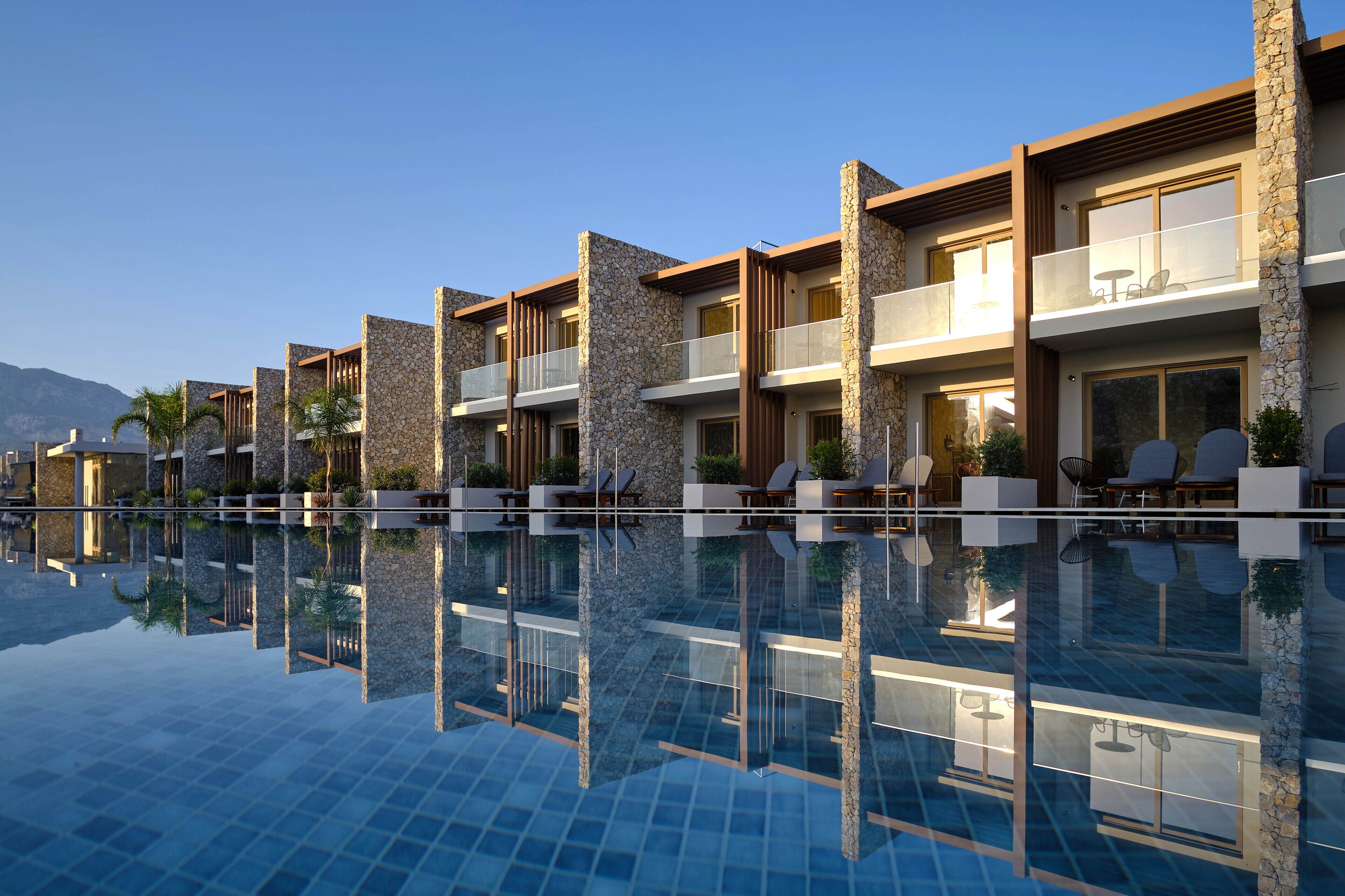 A modern hotel with a swimming pool, stone facade, and outdoor seating areas.