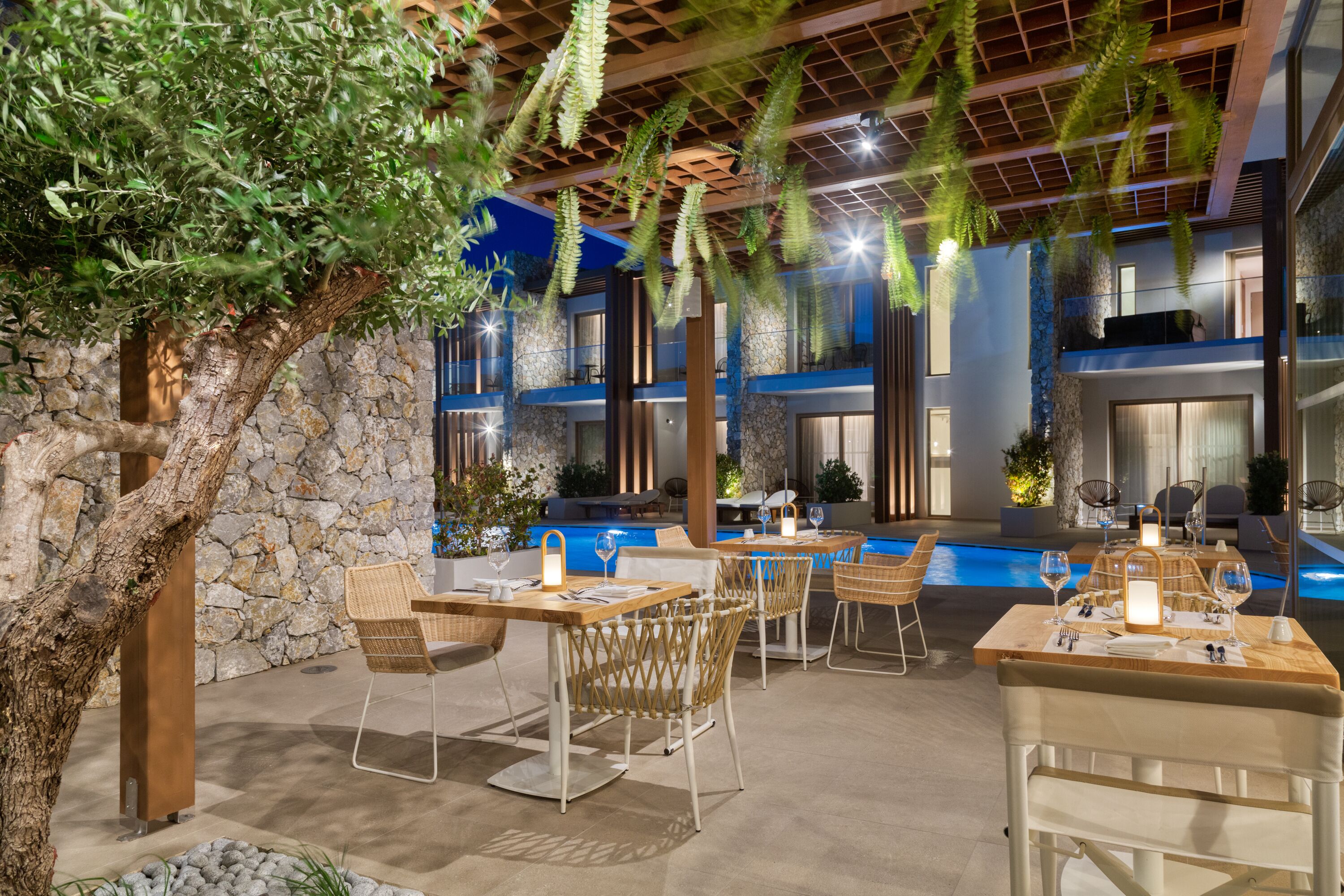 Un área de comedor al aire libre con mesas y sillas, un muro de piedra y una piscina al fondo.