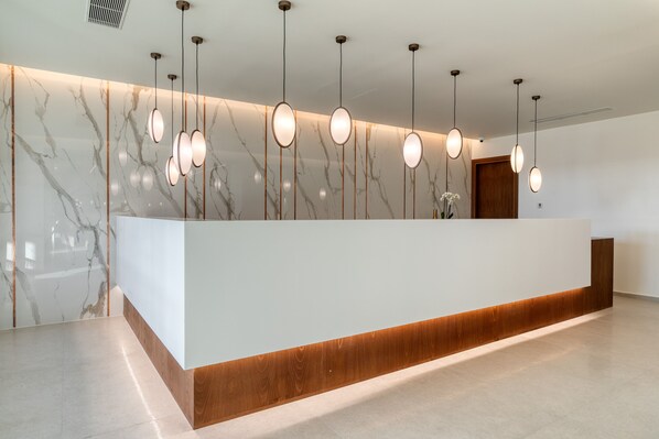A reception desk with a marble wall, wooden accents, and pendant lighting. - Utopia Blu (Kos)