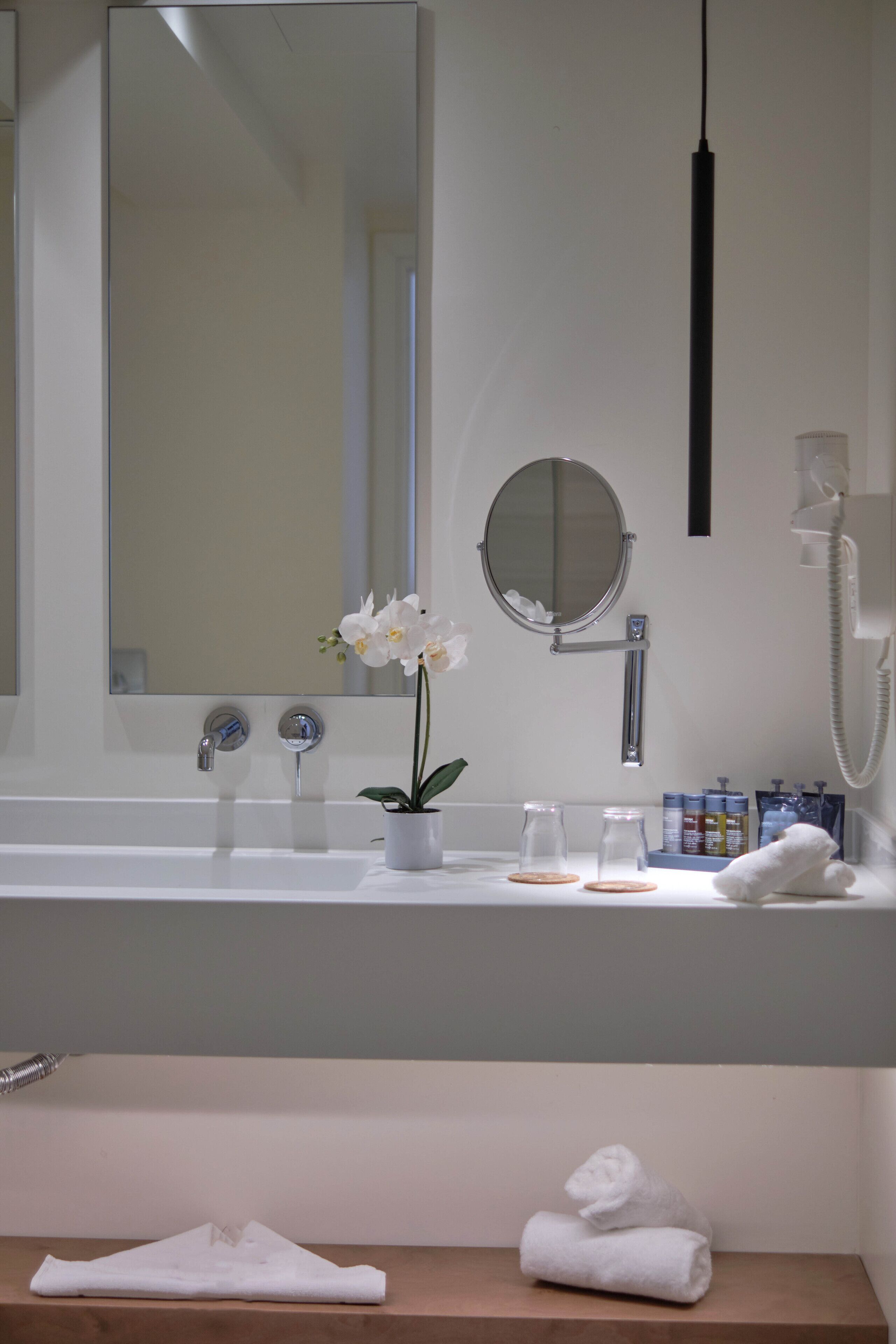 A bathroom with a large mirror, a sink, a telephone, and a small potted orchid.