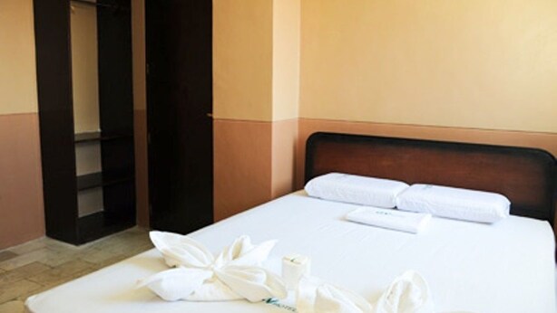 A hotel room with a neatly made bed, a wardrobe, and a small shelf unit. - GV Hotel Ipil (Ipil)