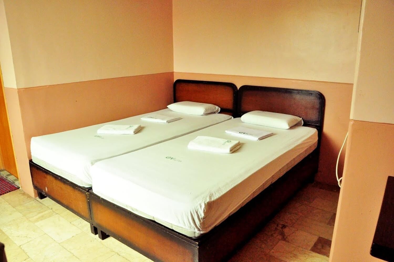 Un letto matrimoniale con lenzuola e cuscini bianchi, una testiera in legno e un pavimento piastrellato.