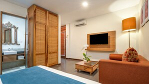 A hotel room with a bed, a sofa, a TV, a mirror, and a bathroom visible through an open door. - Pondok Sari (Kuta)
