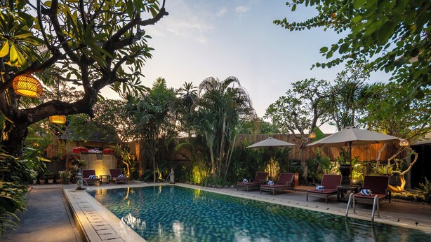 A swimming pool with lounge chairs and umbrellas, surrounded by lush greenery and trees. - Pondok Sari (Kuta)
