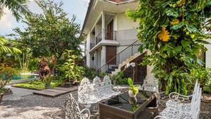 A garden with a pool, outdoor seating, and a staircase leading to a balcony. - Pondok Sari (Kuta)