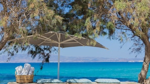 A stone wall with a wicker basket of towels and a large umbrella. - Akti Kastraki Beach (Naxos)