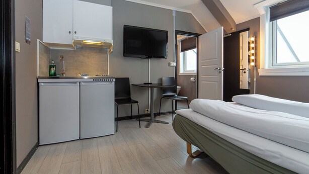 Una habitación compacta con kitchenette, una cama, un televisor y una pequeña mesa con sillas.