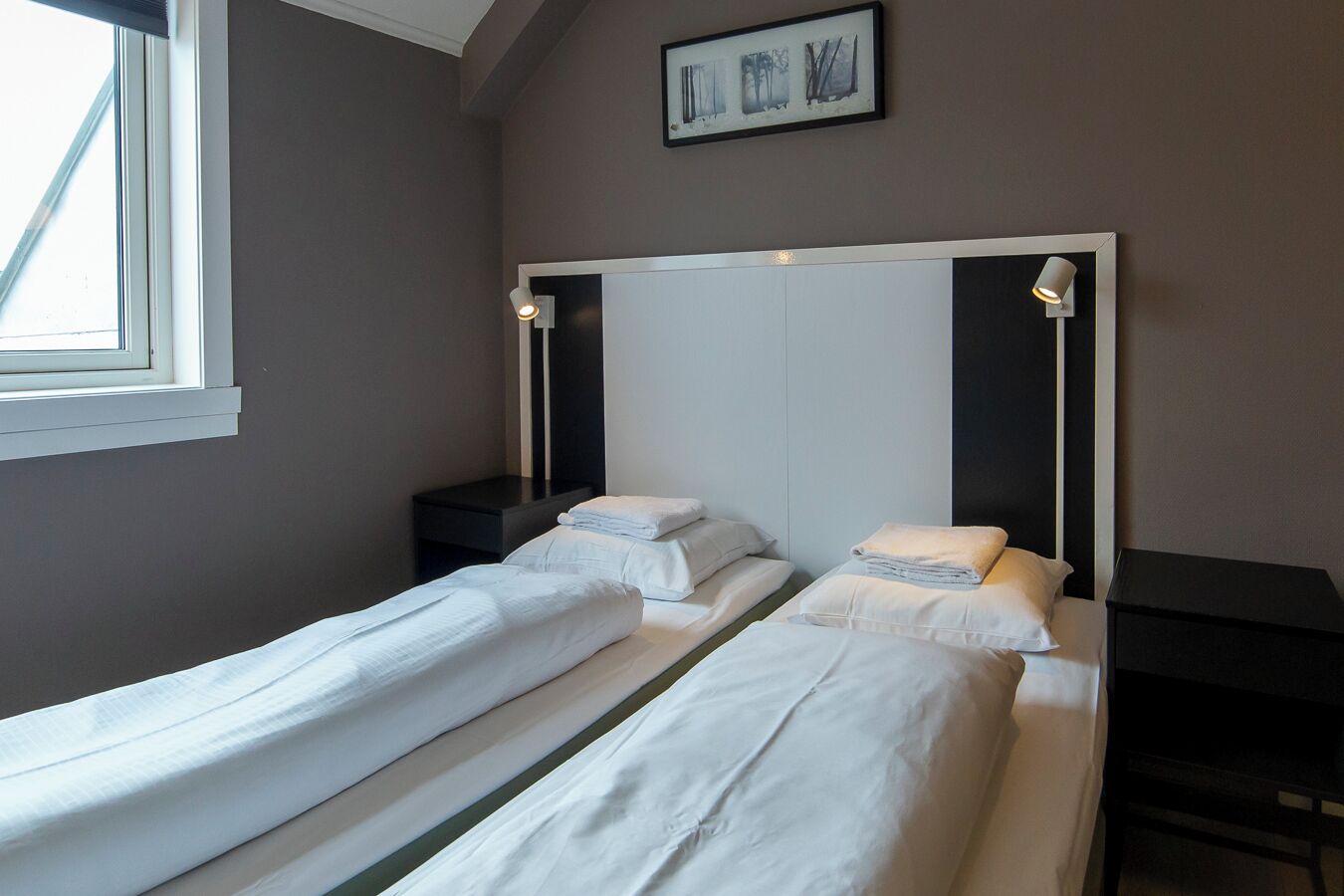 Una habitación de hotel con dos camas individuales, una mesita de noche, una pequeña mesa y una ventana.
