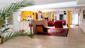 A spacious living area with a red sofa set, a coffee table, and a red accent chair. There is a large potted plant on the left and a red and yellow wall in the background. - Hotel Arheilger Hof (Darmstadt)