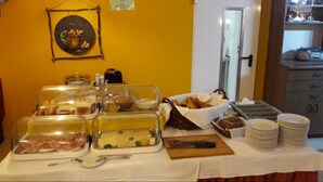 A buffet table with various food items, including meats, cheeses, and breads, in a room with yellow walls and a wooden cabinet. - Hotel Arheilger Hof (Darmstadt)