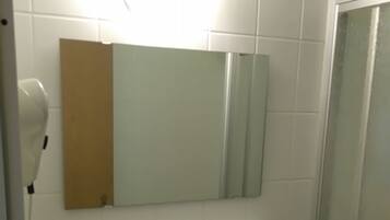 Ein Badezimmer mit einem weißen Waschbecken, einem Spiegel darüber und einer Dusche rechts.