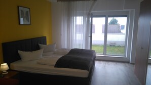 A bedroom with a bed, a nightstand with a lamp, a window with curtains, and a door. - Hotel Arheilger Hof (Darmstadt)