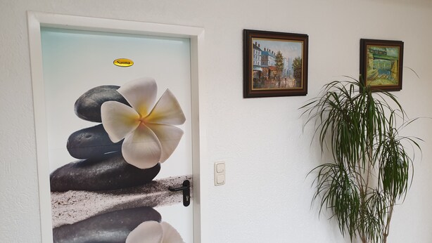 A door with a stone and flower decoration, a wall-mounted light switch, and two framed paintings. - Hotel Arheilger Hof (Darmstadt)