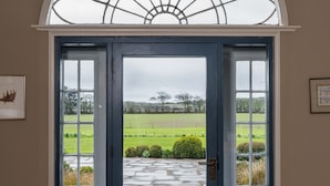 Una puerta azul con un panel de vidrio, que da a un jardín con un camino de piedra y vistas a un campo verde.