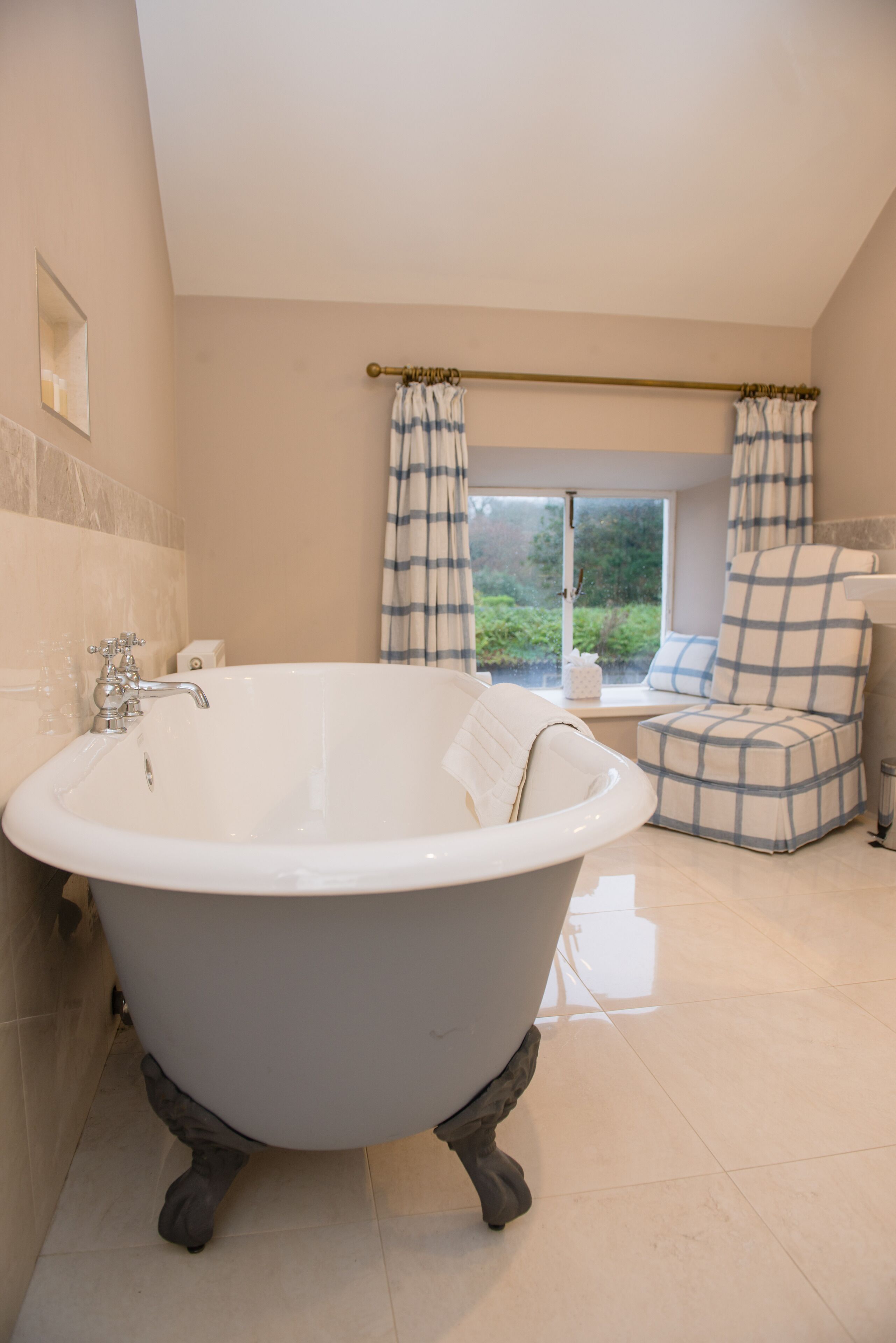 A bathroom with a freestanding bathtub, a window with curtains, and a view of greenery outside.