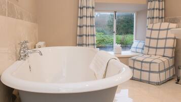 A bathroom with a freestanding bathtub, a window with curtains, and a view of greenery outside.