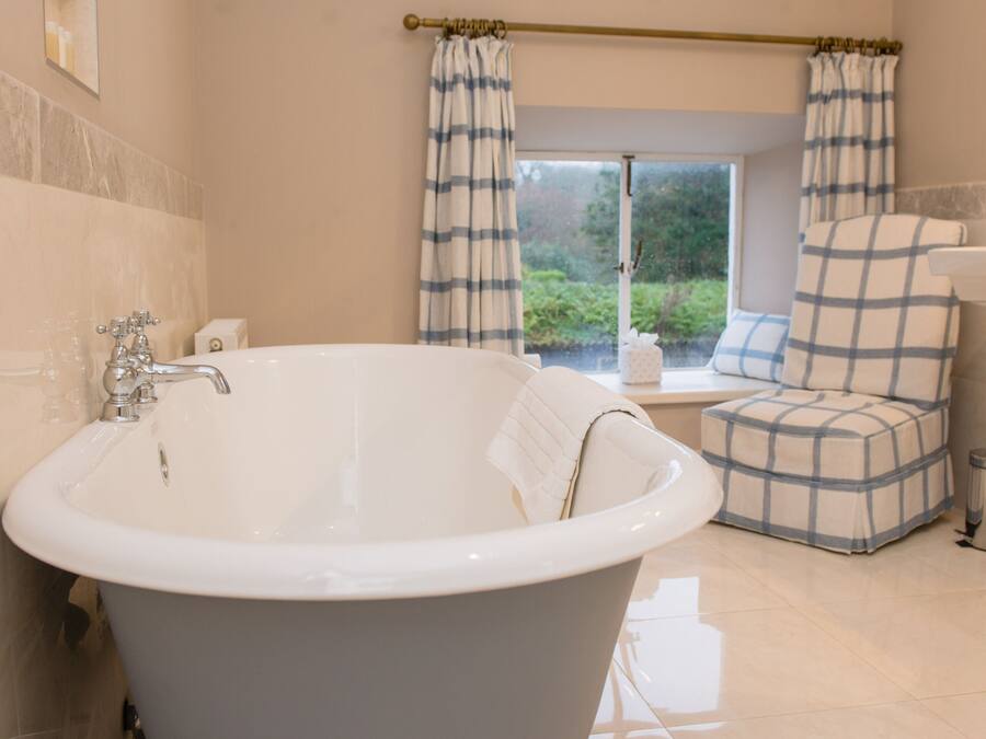 A bathroom with a freestanding bathtub, a window with curtains, and a view of greenery outside.