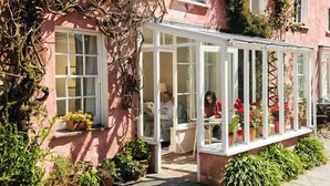 Un edificio rosa con un patio techado, plantas en macetas y una ventana con vista al patio.