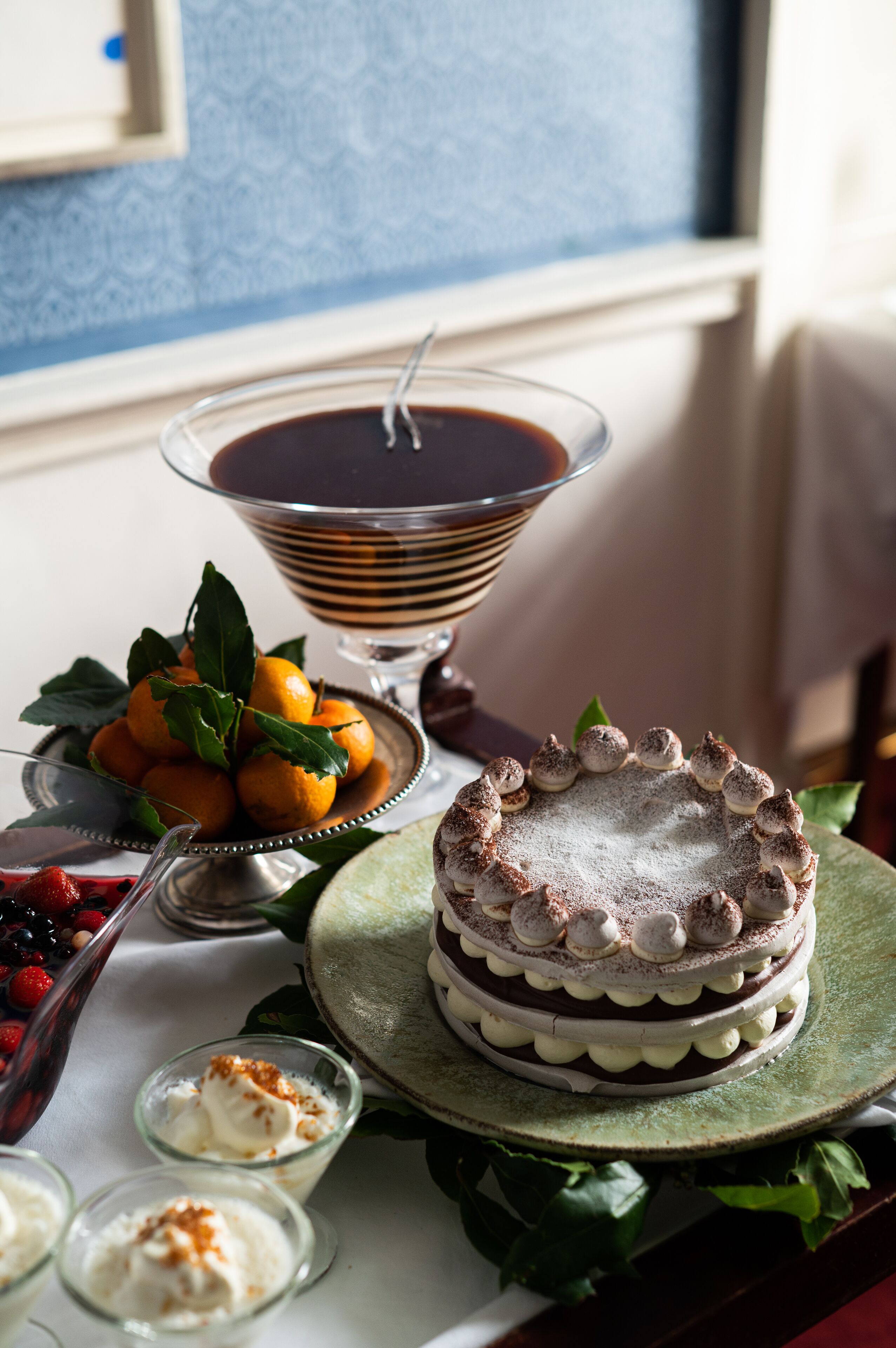 A dessert table with a chocolate cake, a bowl of fruit, and a chocolate drink.