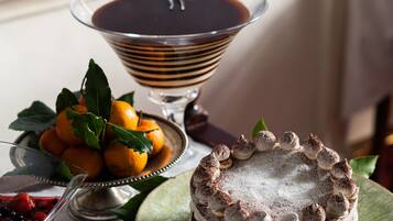 A dessert table with a chocolate cake, a bowl of fruit, and a chocolate drink.