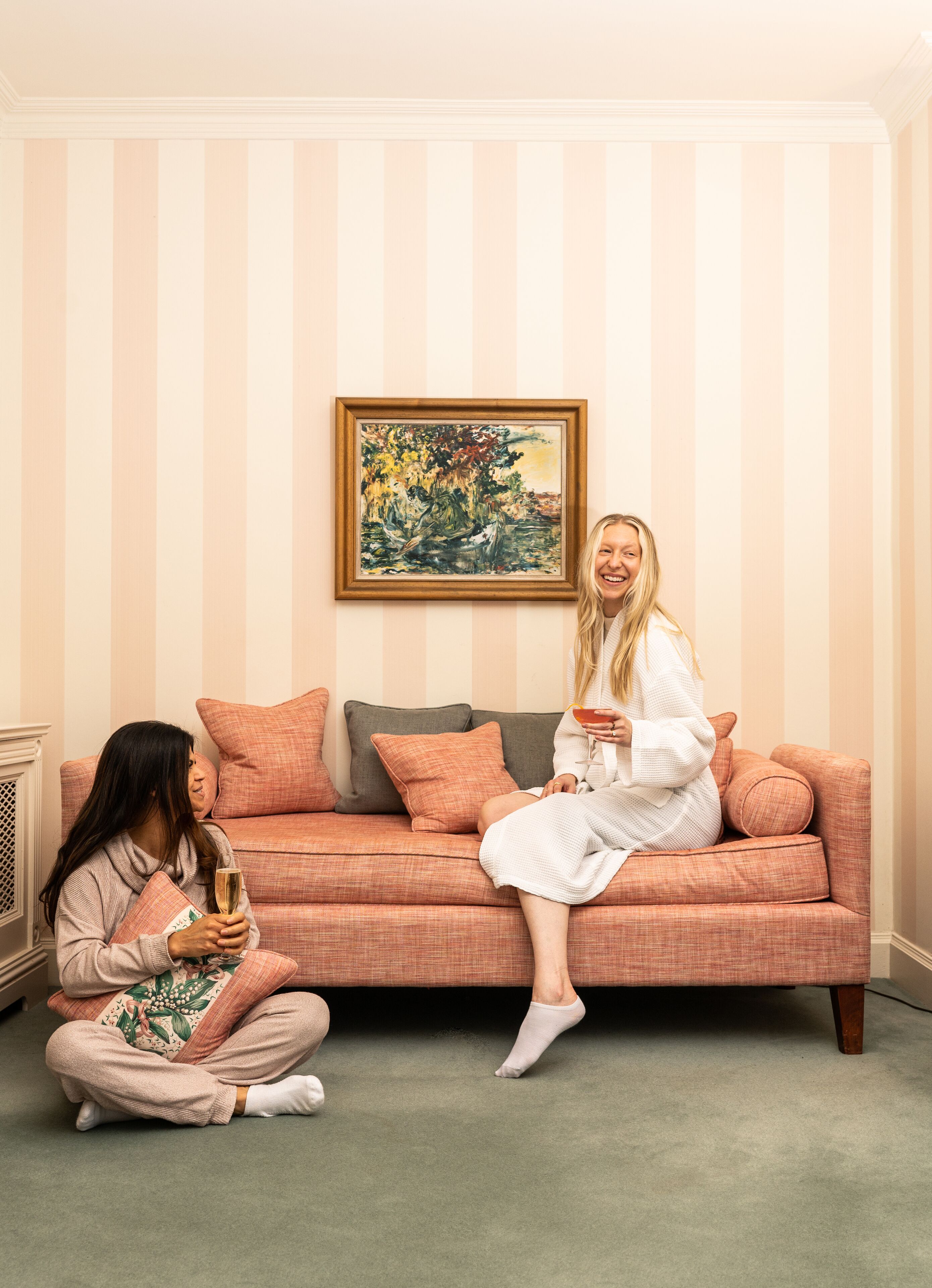 Una habitación con una pared a rayas, un cuadro enmarcado y un sofá rosa con cojines.