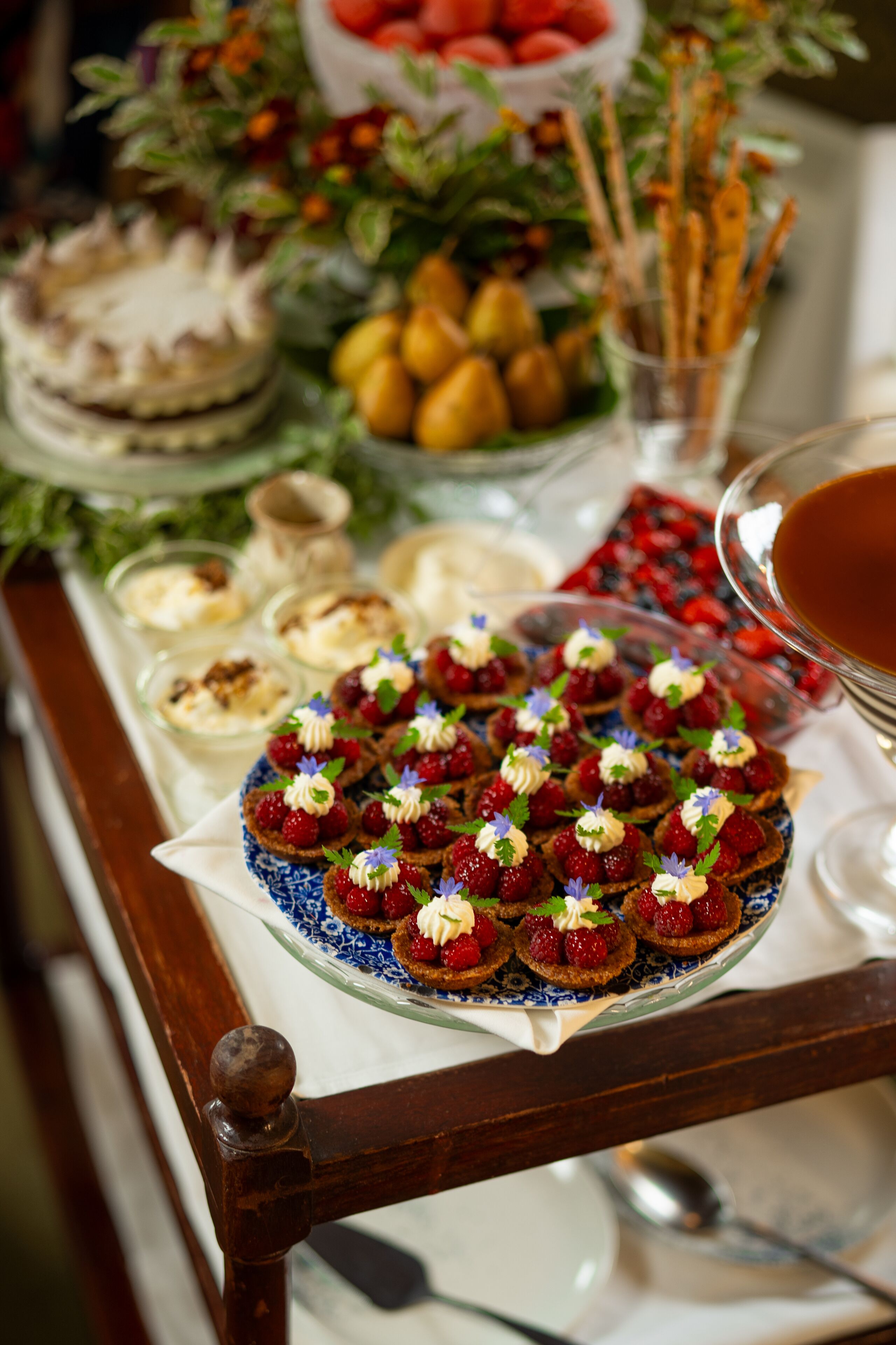 A buffet table with various food items including a plate of decorated pastries, a bowl of strawberries, and a glass of tea.