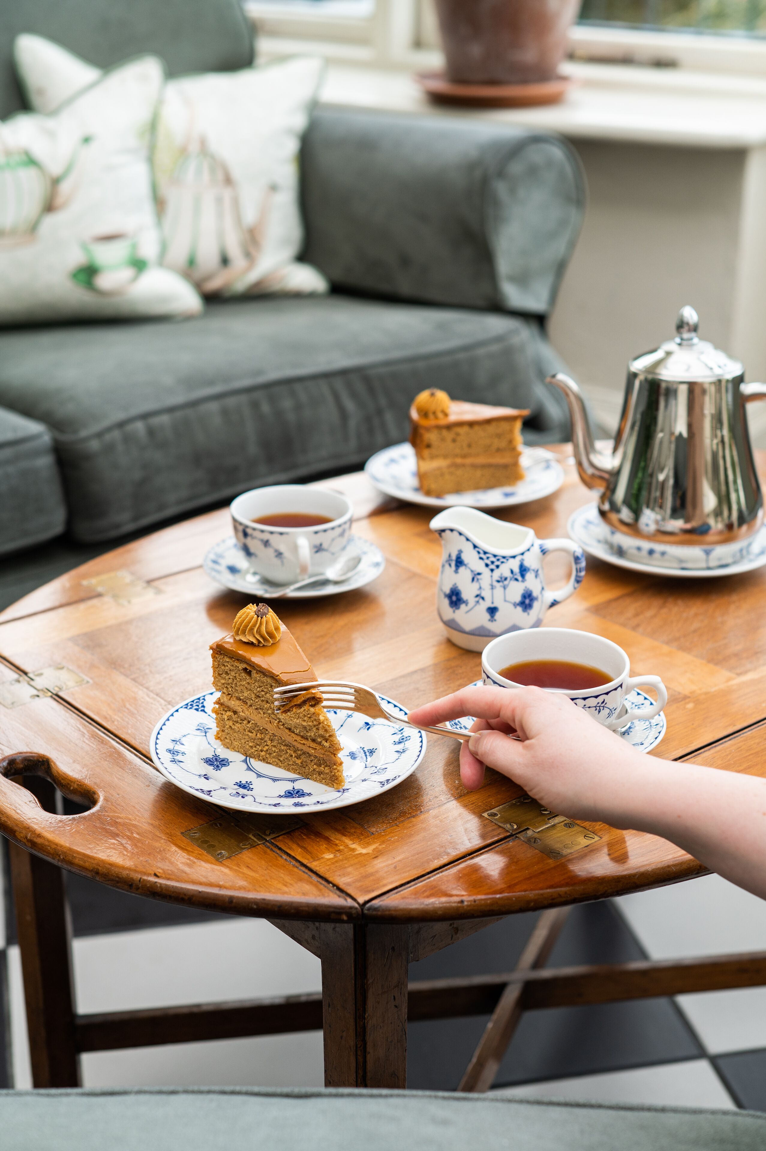A round wooden table with a slice of cake, a cup of tea, and a teapot.