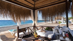 A beachside lounge with a wooden deck, lounge chairs, a table with a fruit bowl, and a view of the ocean. - Limak Limra Hotel & Resort  (Kemer)
