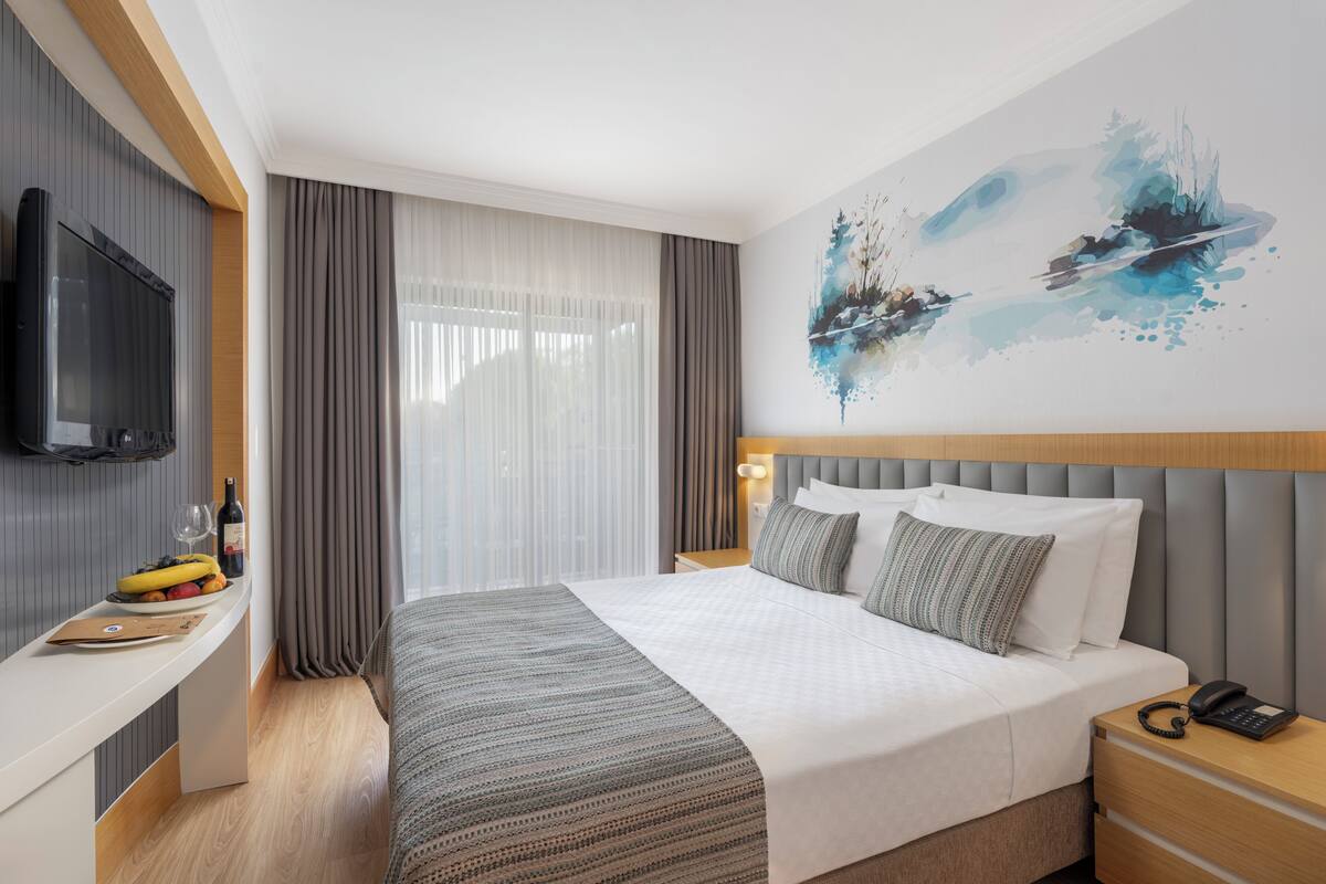 A hotel room with a bed, a TV, a bedside table with a phone, a nightstand, and a wall painting.