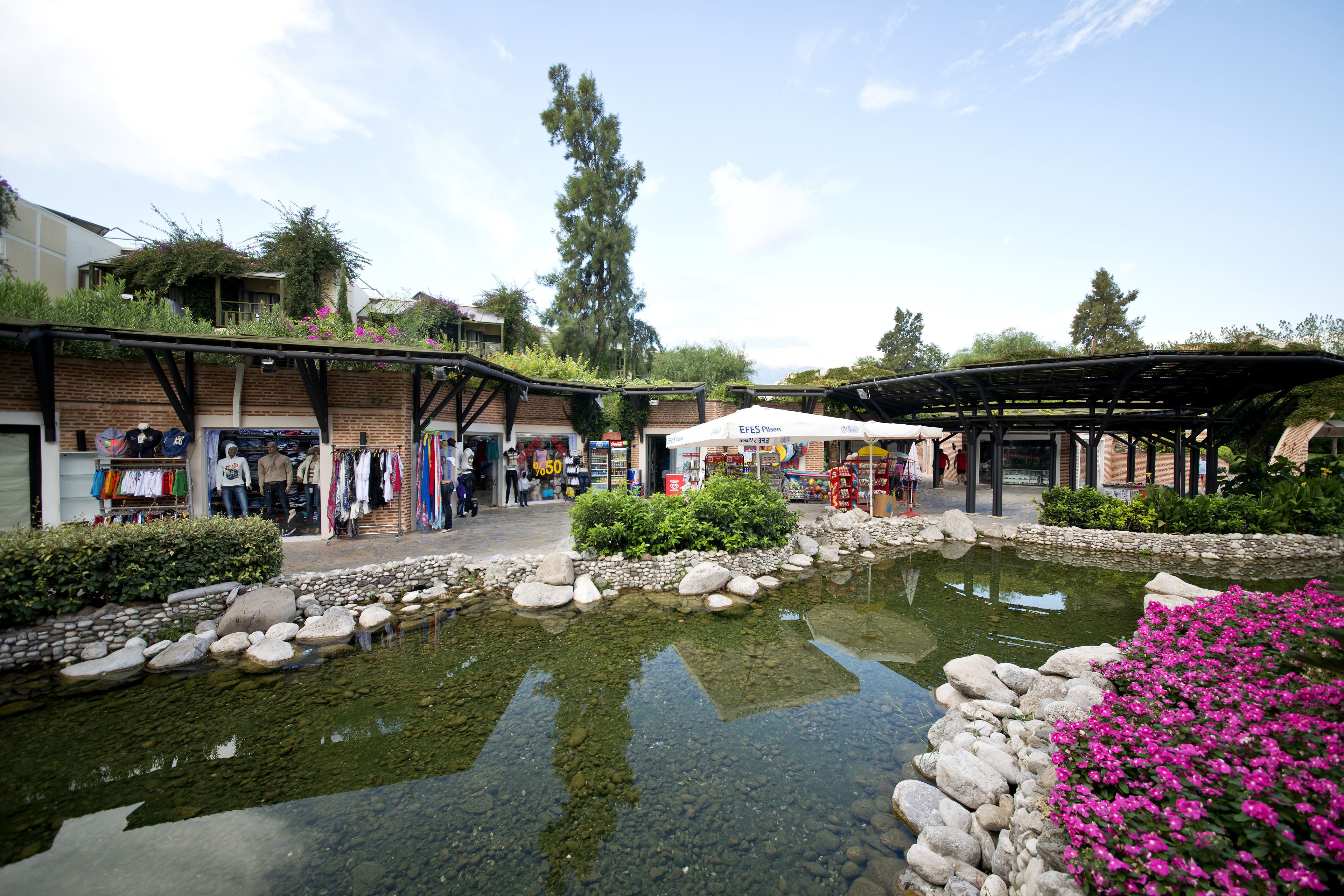 A courtyard with a pond, shops, and a covered seating area.