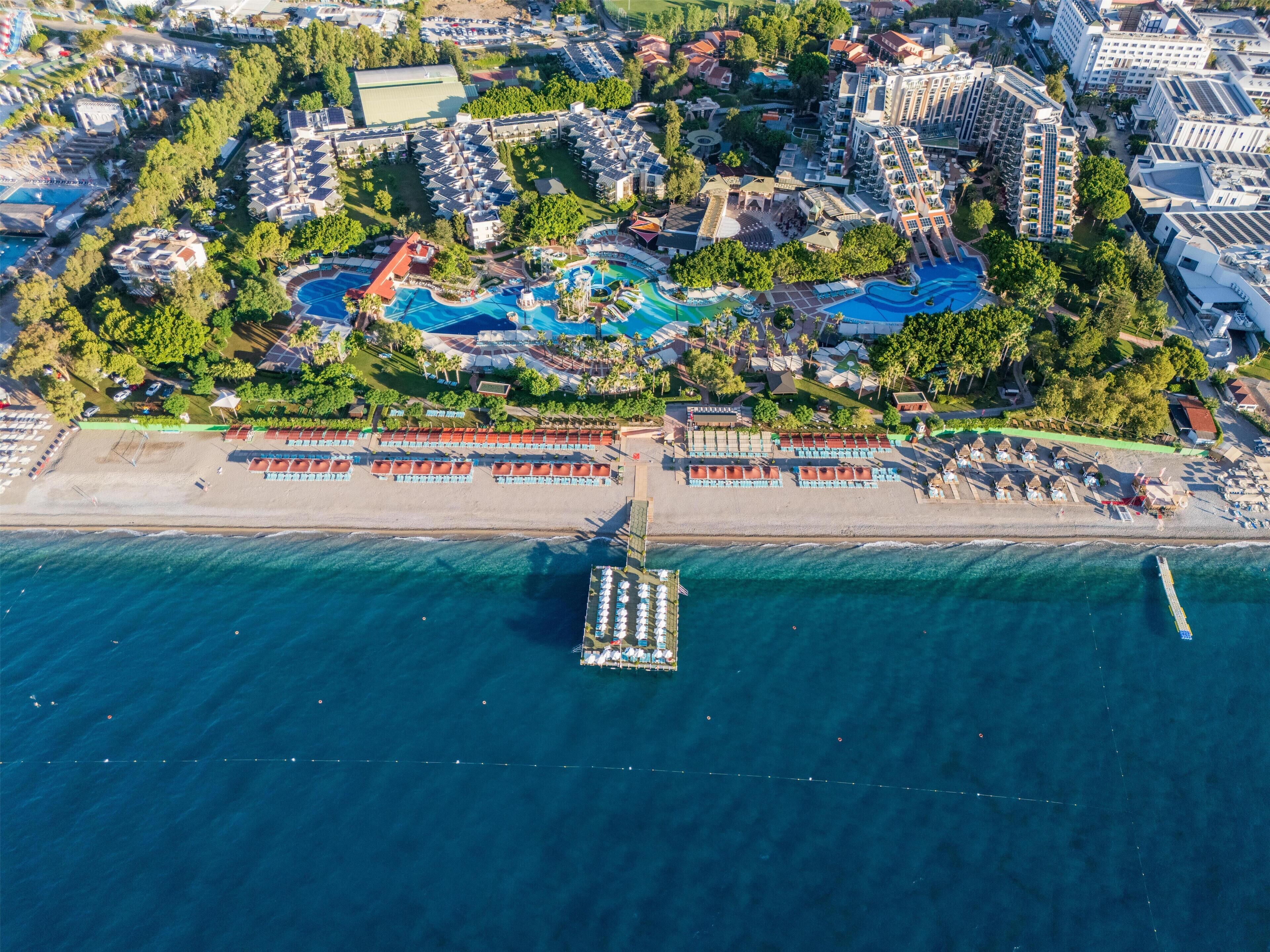 An aerial view of a resort with multiple swimming pools, a beach area, and a dock.